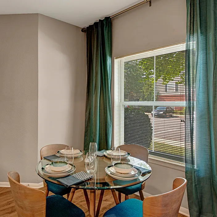 Dining nook with round glass table, blue cushioned chairs, and natural light from large window