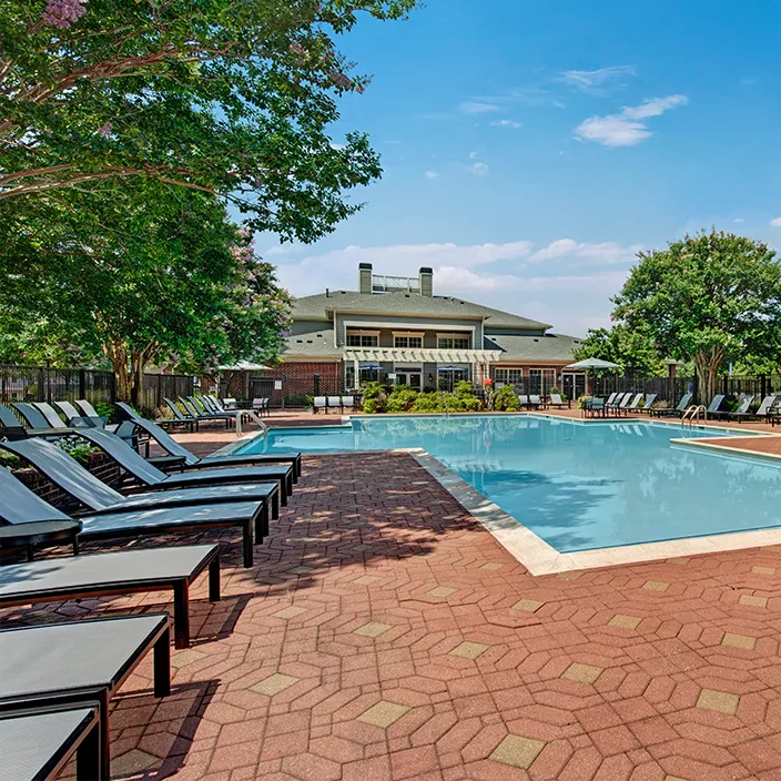 Outdoor pool area with lounge chairs and clubhouse under a clear blue sky