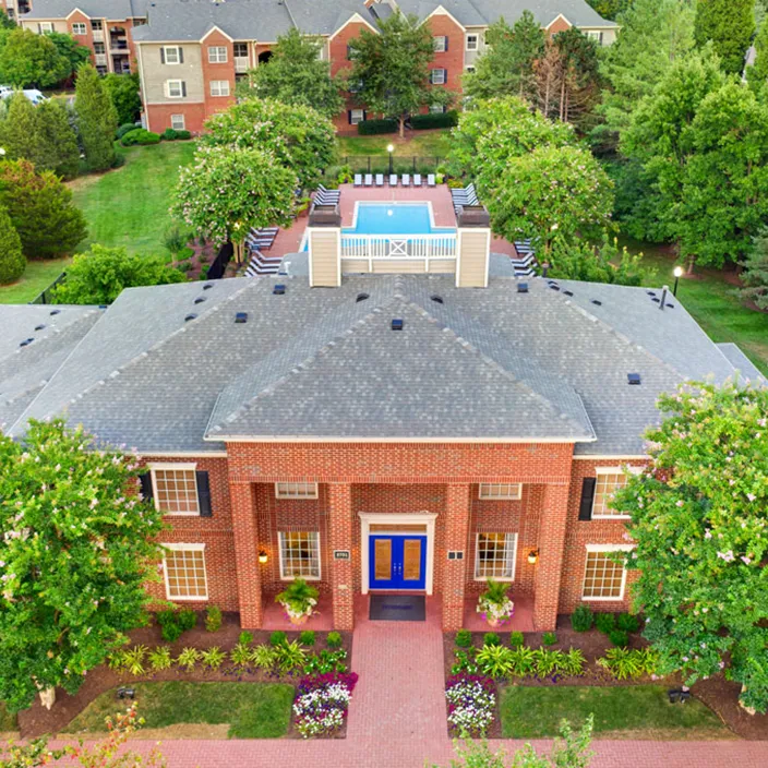 Elevated view of clubhouse with landscaped grounds, rooftop pool, and lush green surroundings