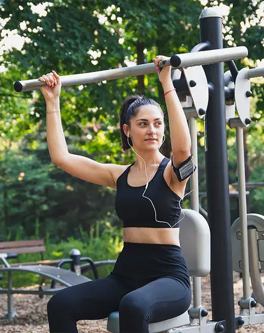 Woman practicing upper body workout on park fitness trail, surrounded by nature