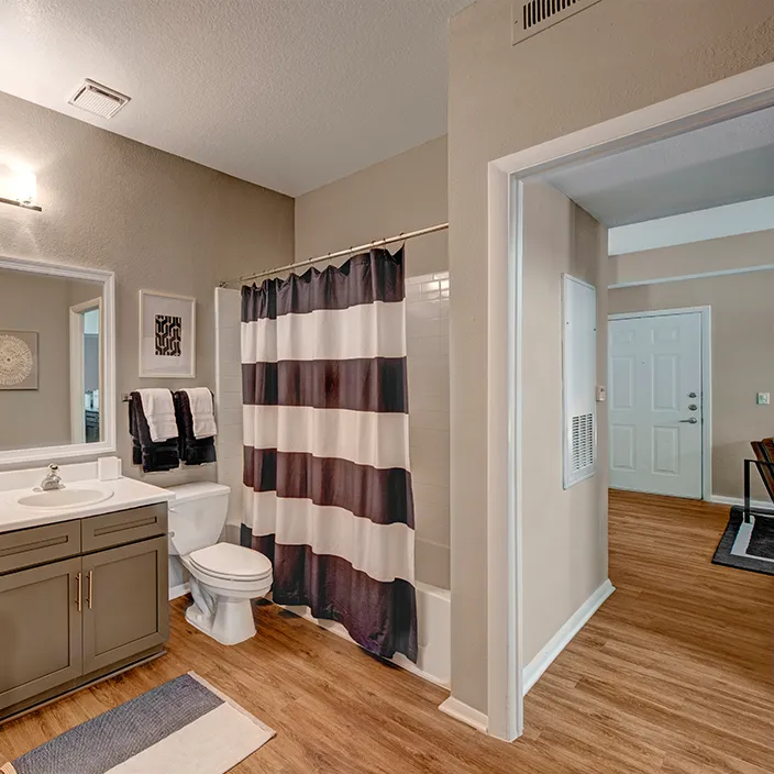 Modern bathroom with large mirror, stylish cabinetry, and striped shower curtain in upscale apartment