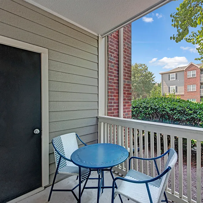 Cozy patio with seating, white railing, and garden view in stylish apartment community