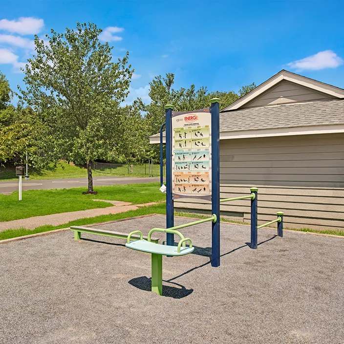 Apartment complex outdoor gym with exercise equipment and instructional signs under open sky