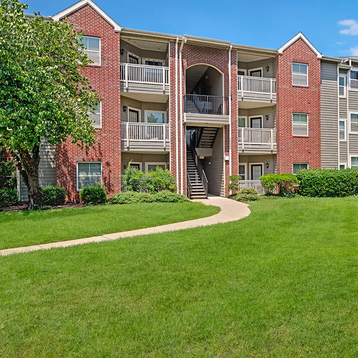 Apartment building exterior with brick facade, balconies, and lush green lawn in landscaped setting