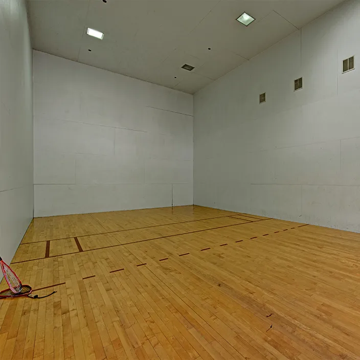 Indoor racquetball court with wooden flooring and high ceilings in apartment complex amenity area